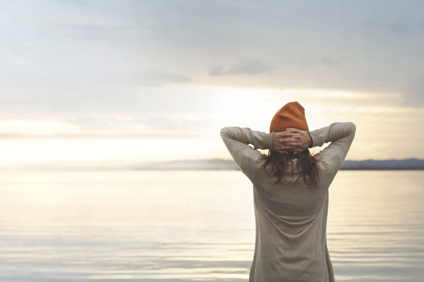 frau_steht_mit_verschraenkten_armen_hinter_dem_kopf_und_blick_auf_das_weite_meer